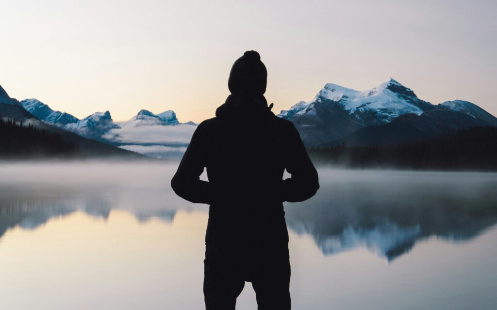 A solitary figure in reflection, observing a tranquil and perfectly clear alpine lake at sunrise, illustrating the mental clarity and stillness of mindfulness practice.