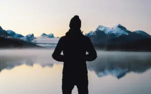 A solitary figure in reflection, observing a tranquil and perfectly clear alpine lake at sunrise, illustrating the mental clarity and stillness of mindfulness practice."